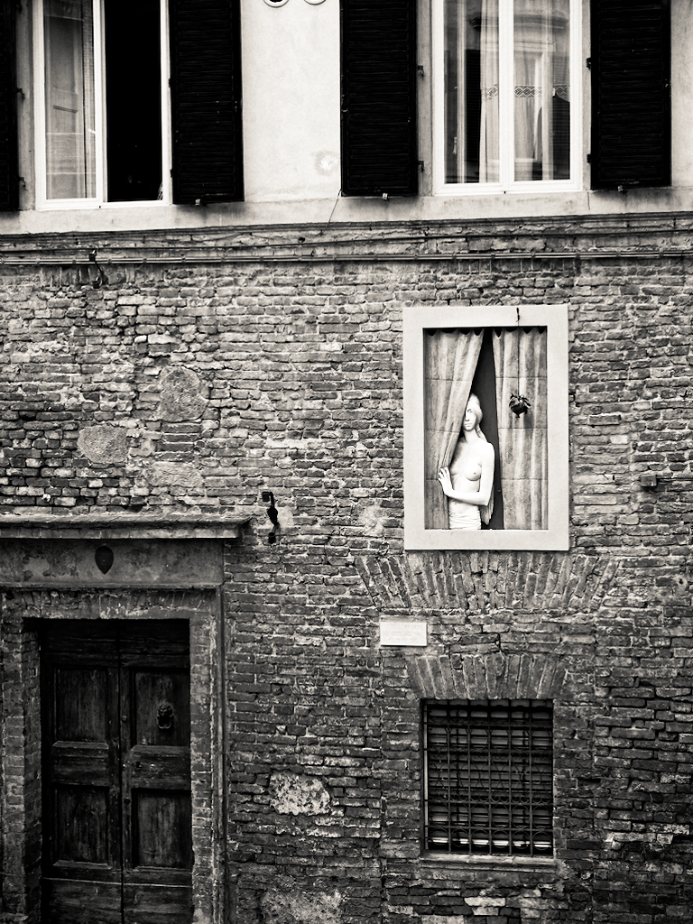 Mannequin behind a curtain in the window of an old Italian brick building